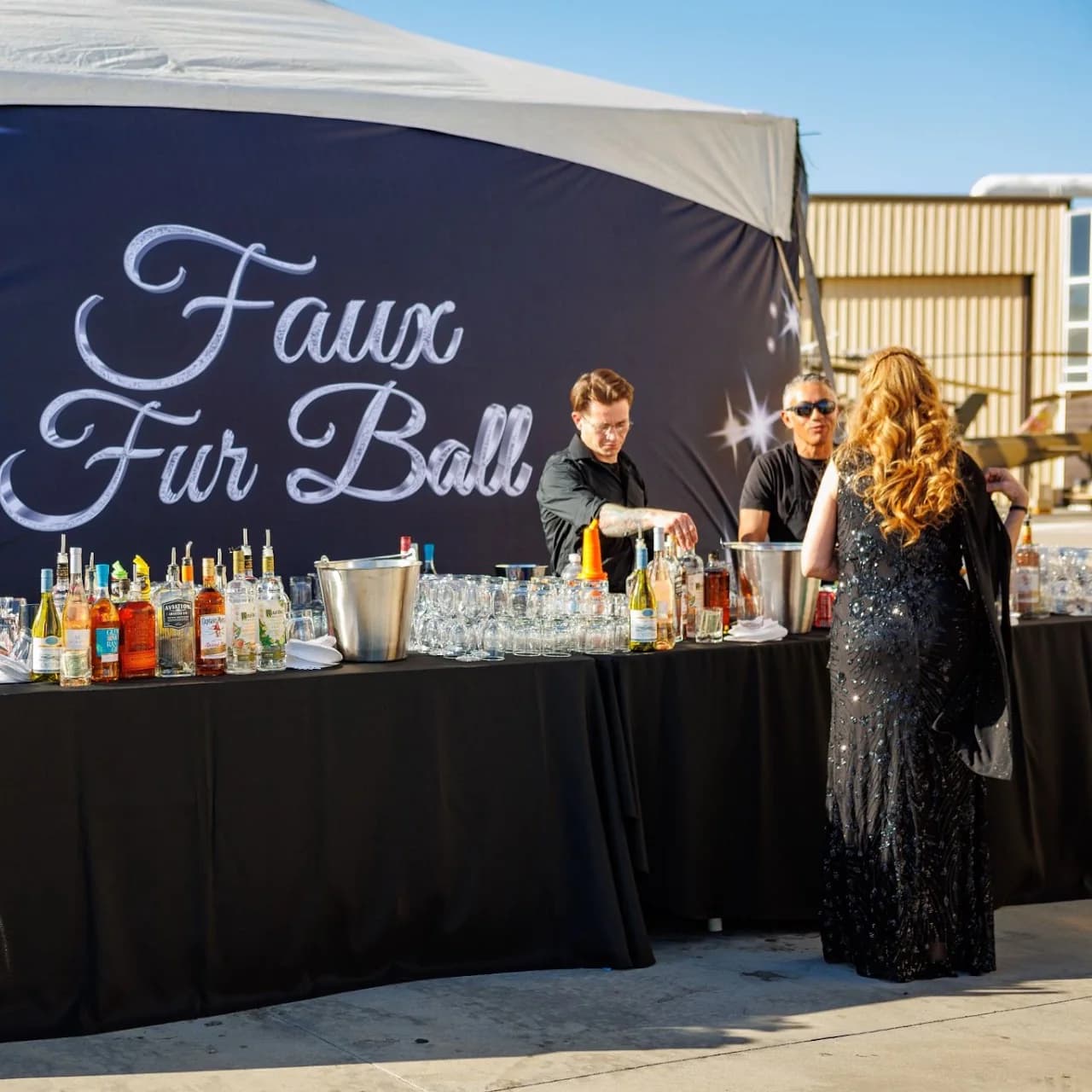 Guests visiting an outdoor hospitality station with a large event backdrop