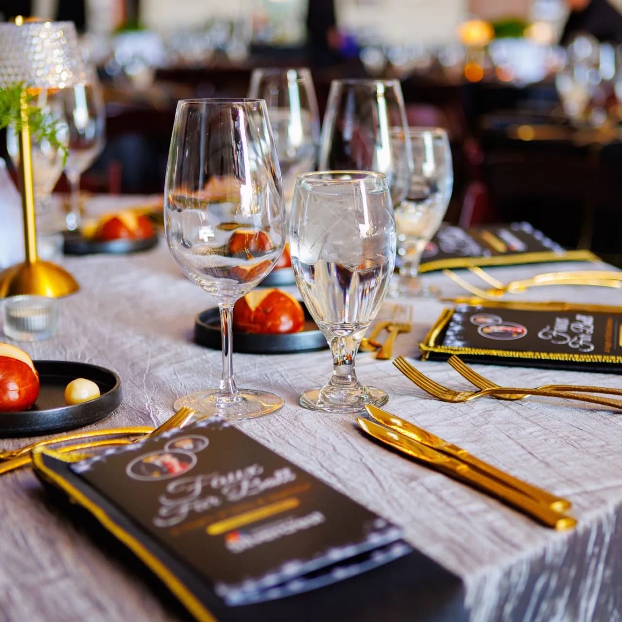 Formal place setting with glassware, printed programs, and gold flatware