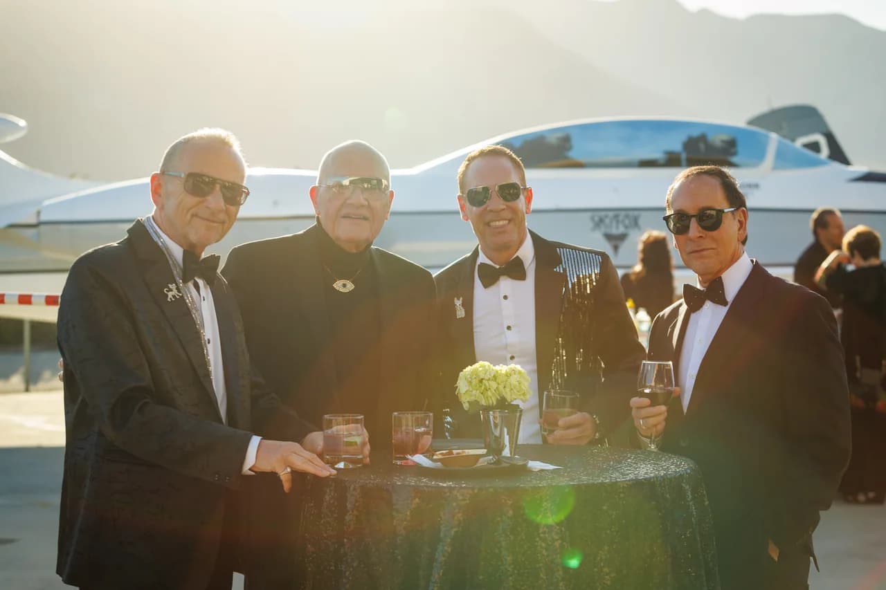 Four formally dressed guests gathered around a cocktail table outdoors
