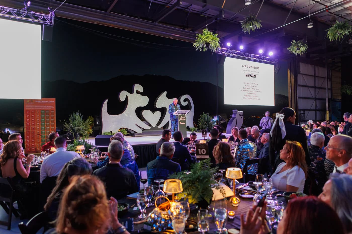 Speaker addressing guests at a formal event with tables and stage lighting
