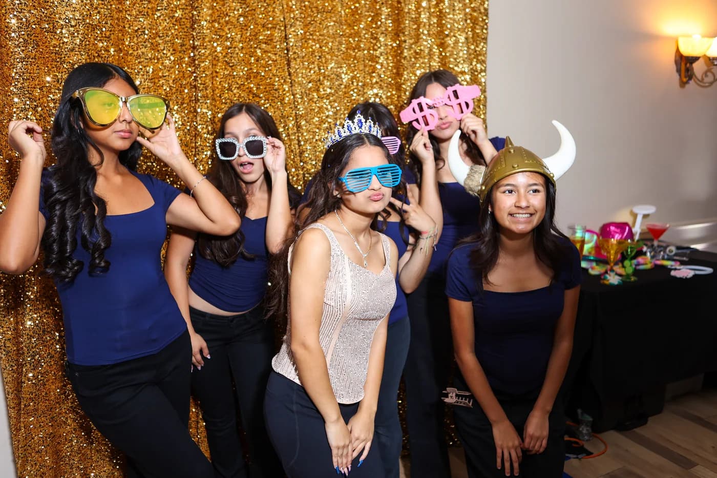 Guests posing with playful props against a gold sequin photobooth backdrop