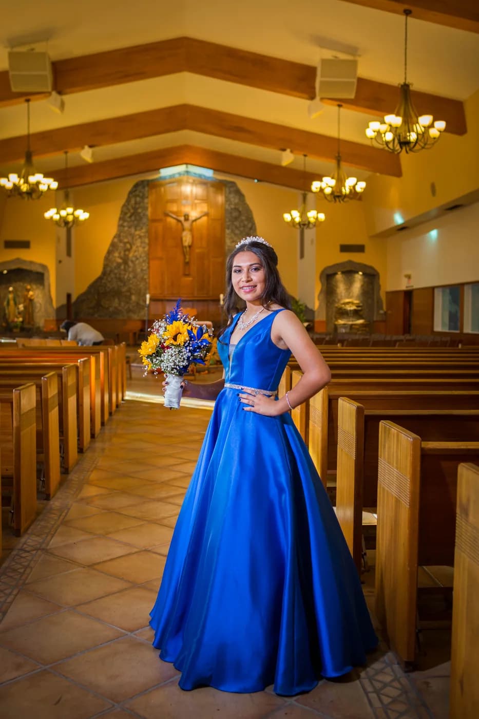 Quinceañera in a royal blue gown holding a bouquet inside a church
