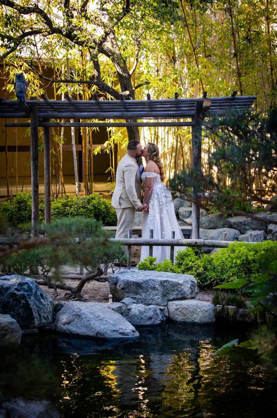 Newlyweds sharing a kiss in a garden framed by trees and bamboo