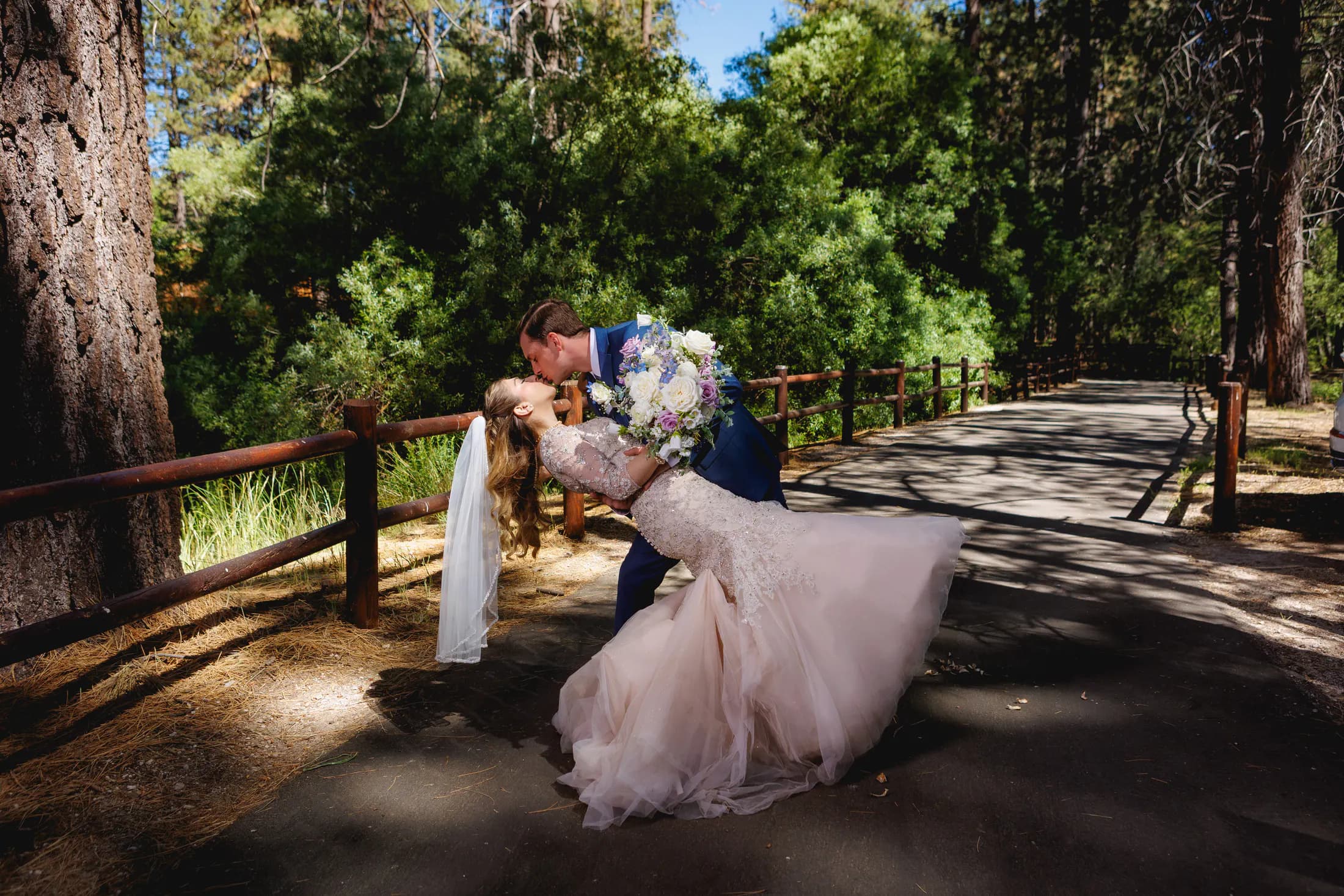 Newlyweds sharing a kiss on a tree-lined forest road