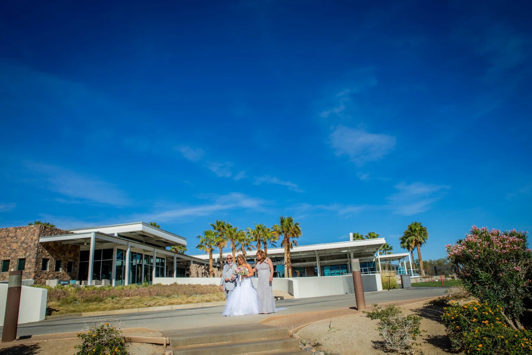 Stephen and Heather walking with two guests outside Escena Golf Club beneath a deep blue sky