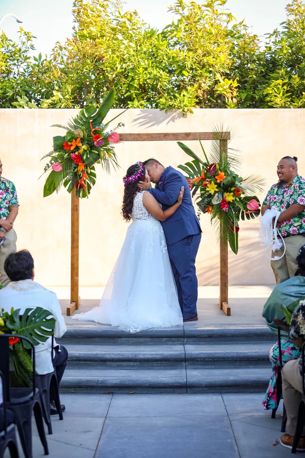 Jed and Azalea sharing a kiss beneath the ceremony arch