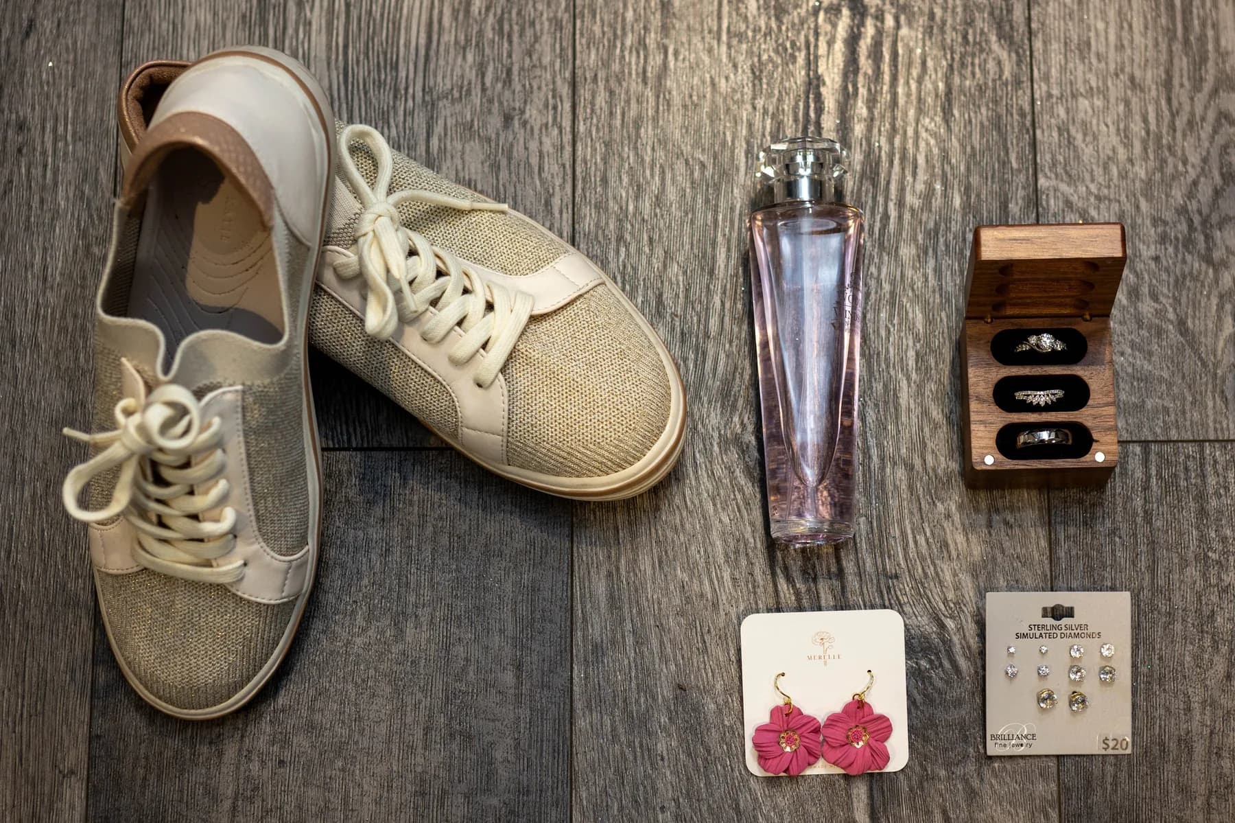 Shoes, fragrance, rings, and small wedding details arranged on a dark surface