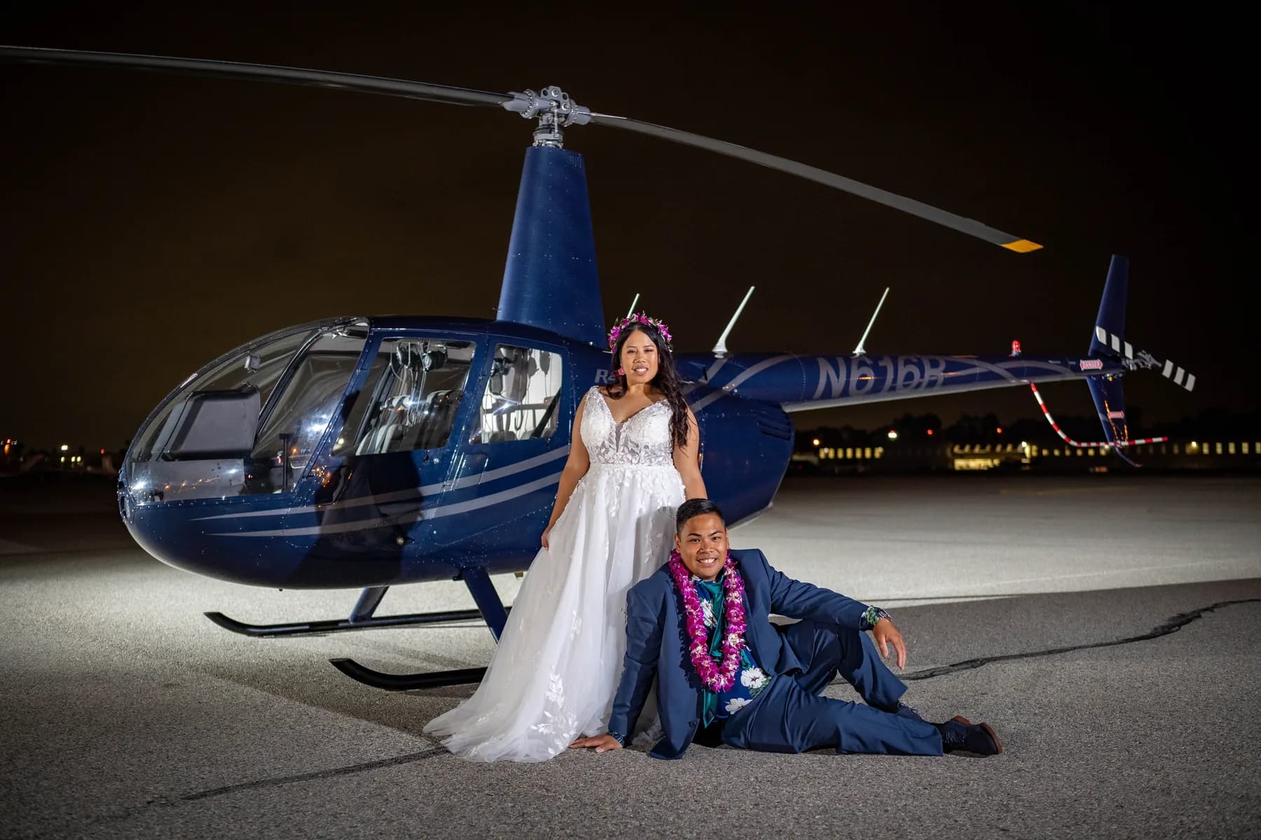 Jed and Azalea illuminated beside the blue helicopter on the airfield at night