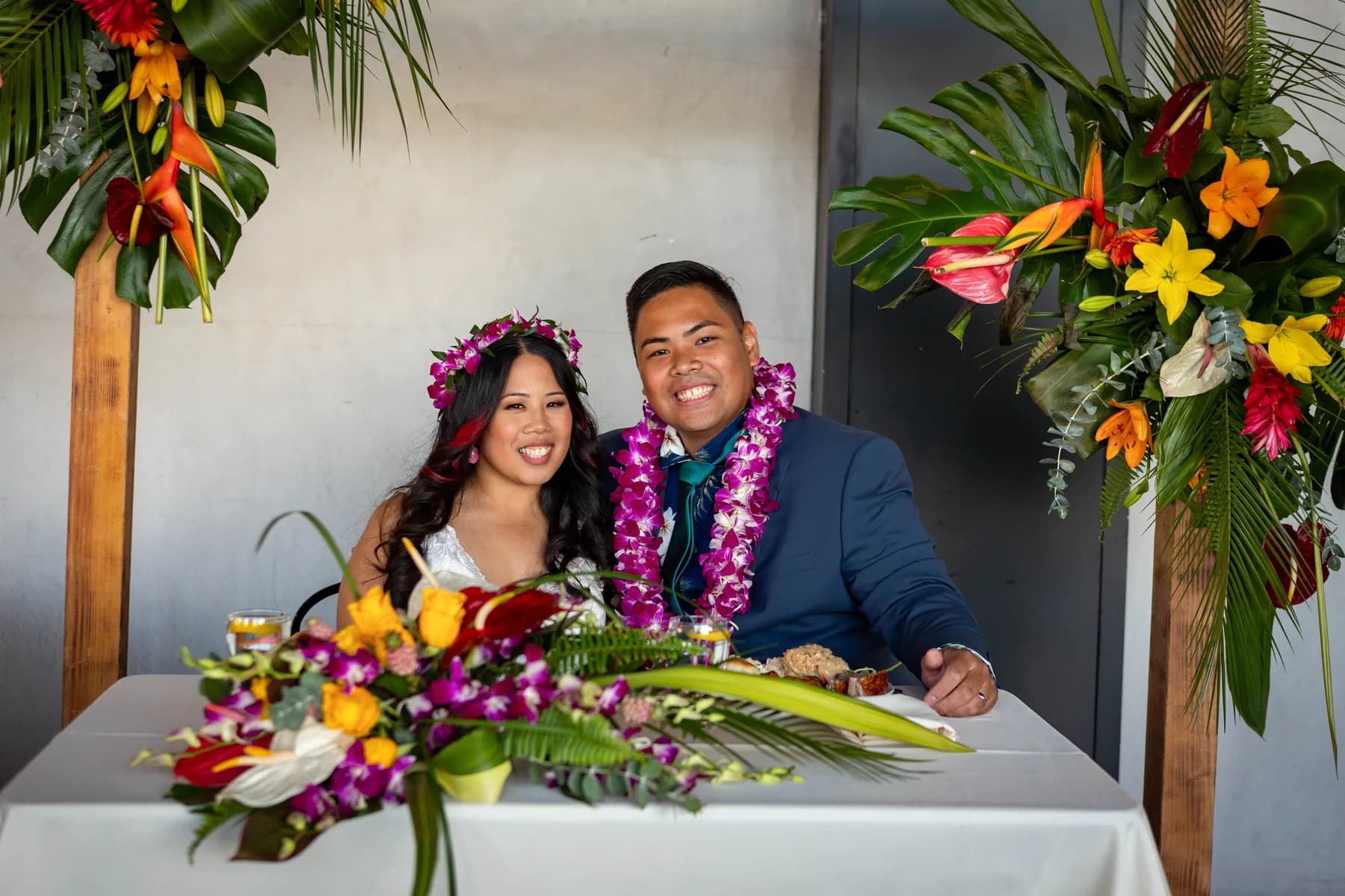 Jed and Azalea seated together beneath the tropical floral arch