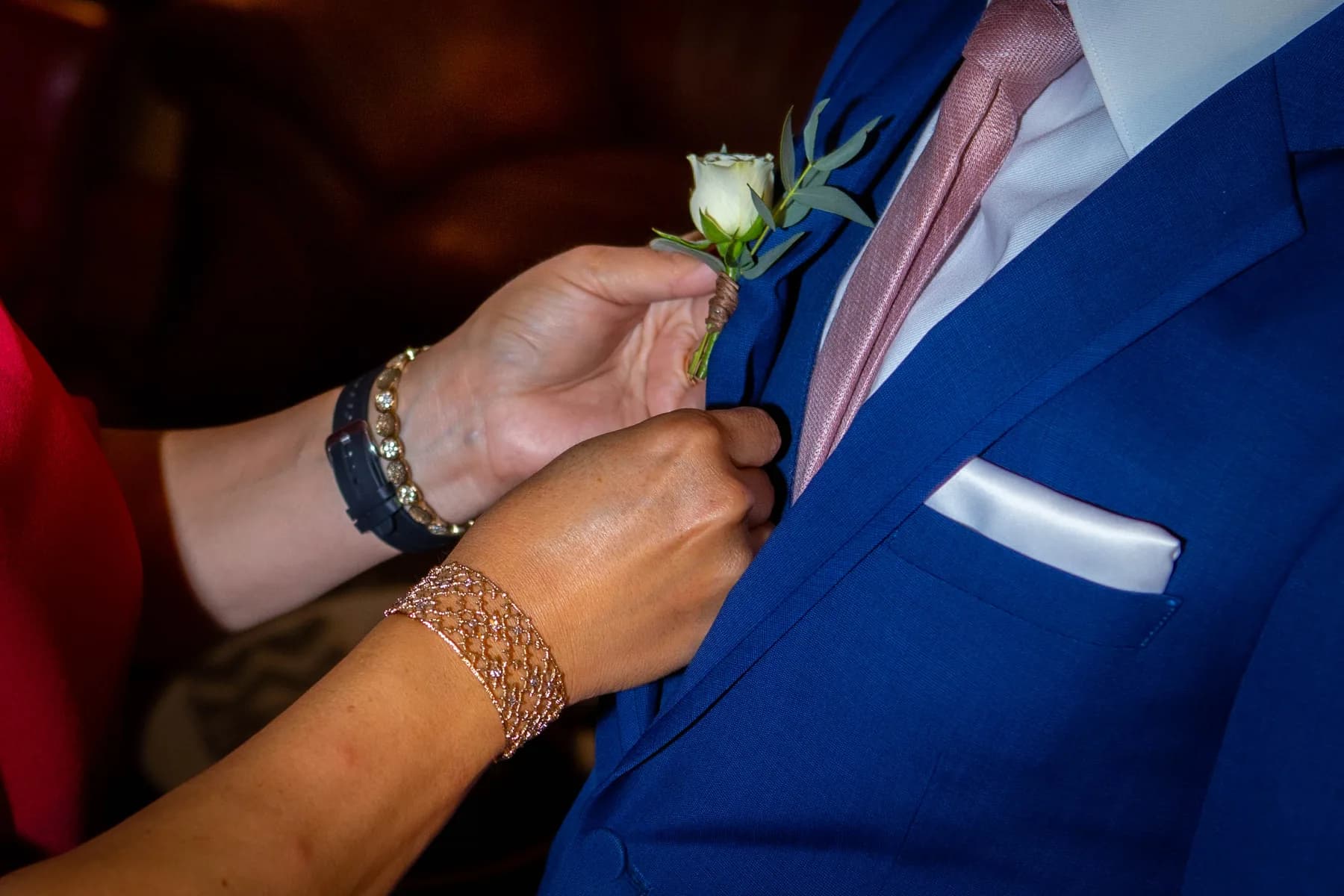Hands fastening a white boutonniere to a blue suit