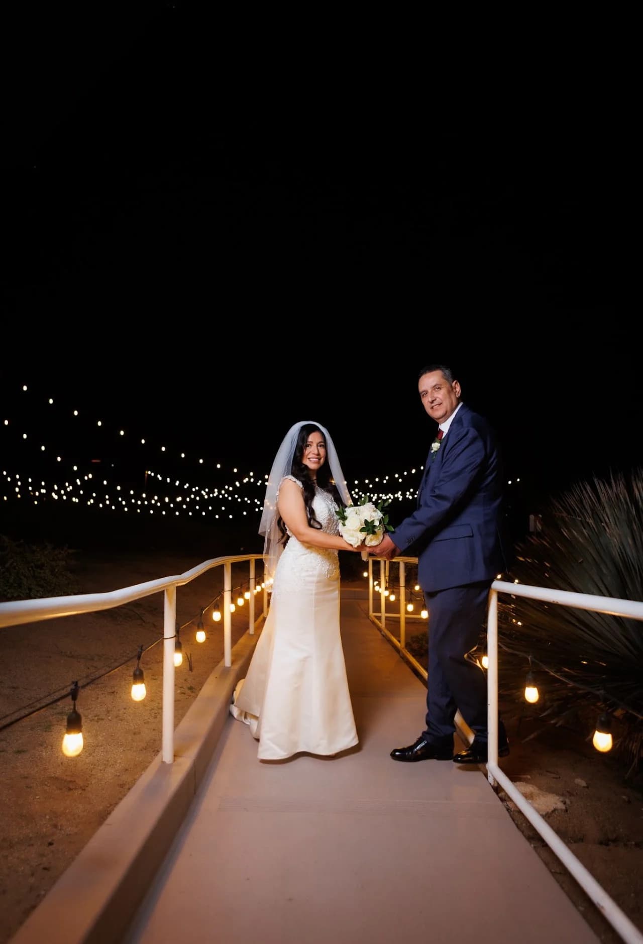 Full-length couple portrait beneath string lights
