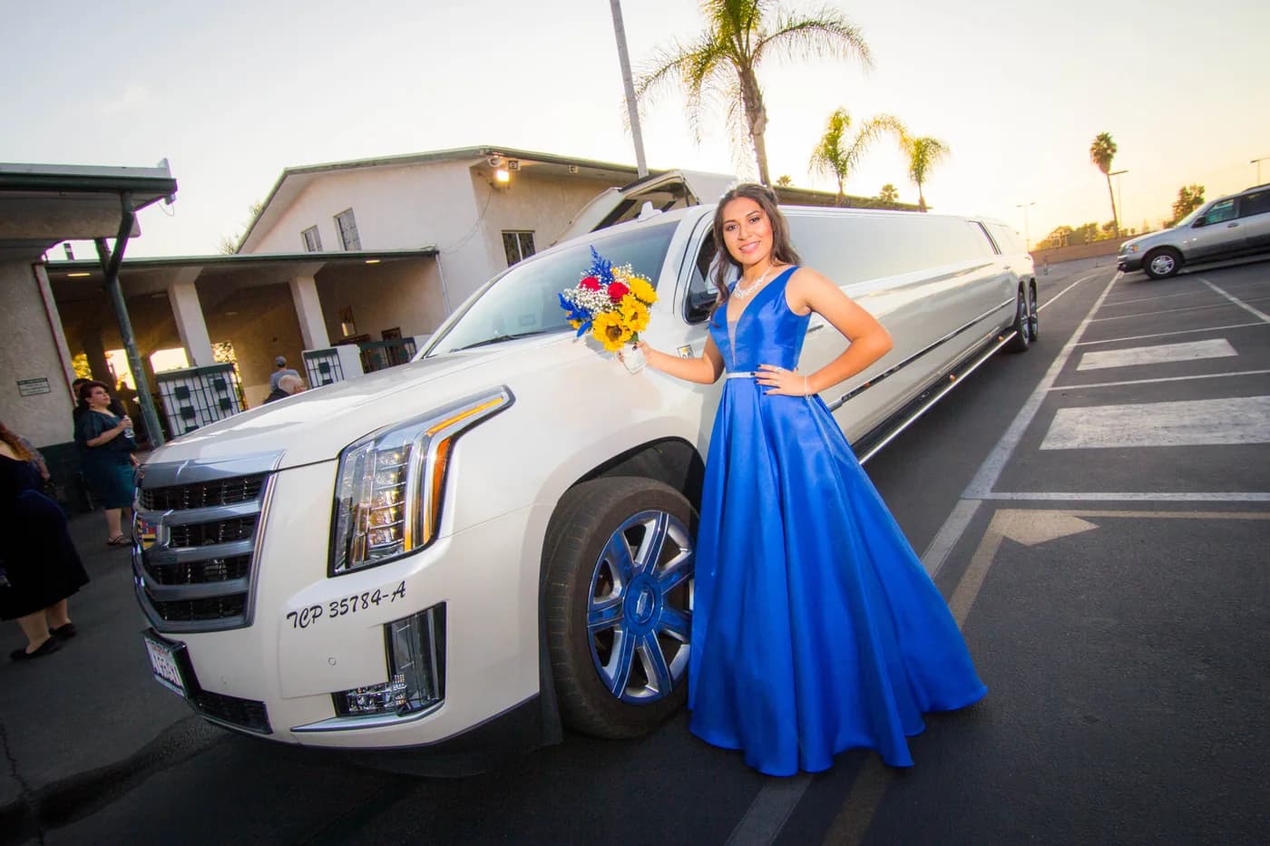 Quinceañera in a royal blue gown posed beside a white limousine