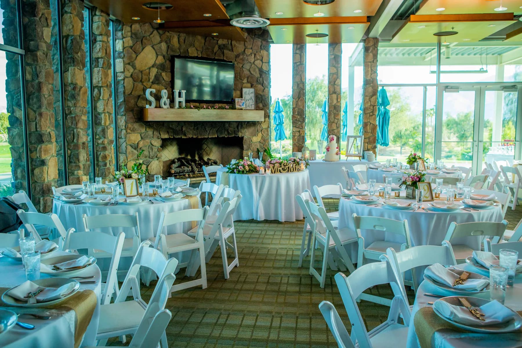 Indoor reception room with round tables, large windows, and a stone fireplace