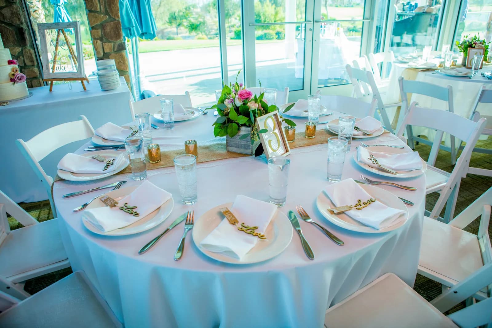 Round wedding reception table set beside large windows at Escena Golf Club