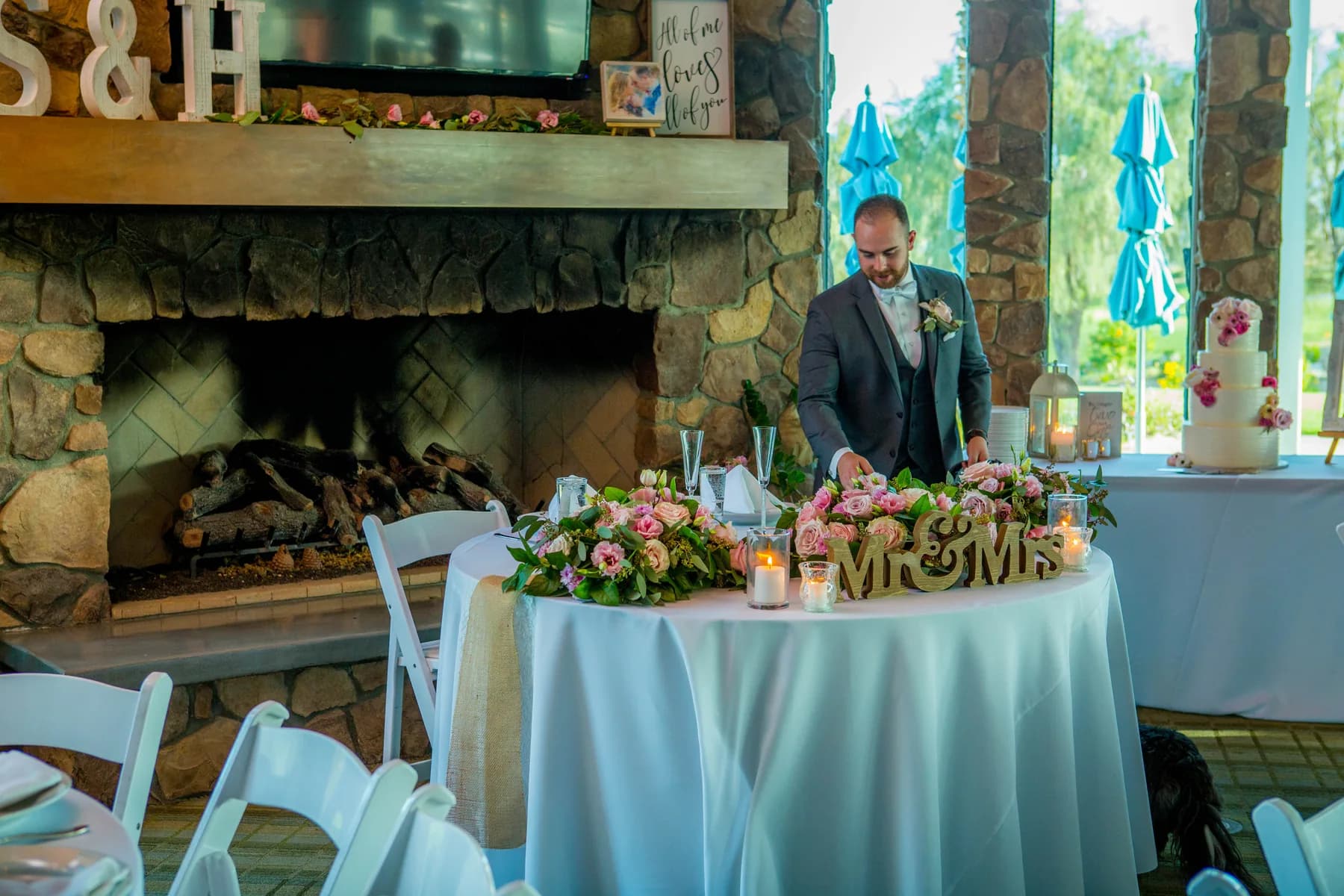 Sweetheart table decorated with pink flowers in front of a stone fireplace