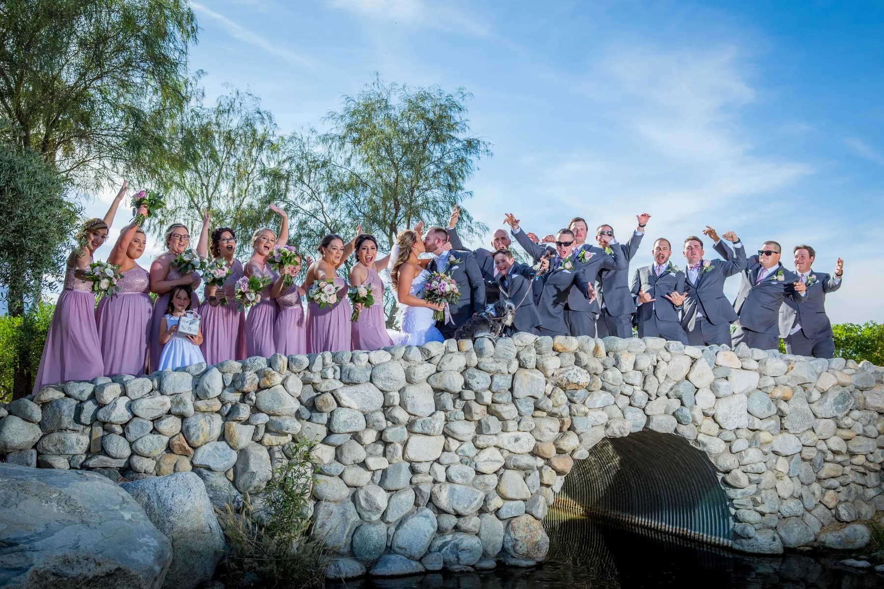 Wedding party standing above a stone bridge on the grounds of Escena Golf Club