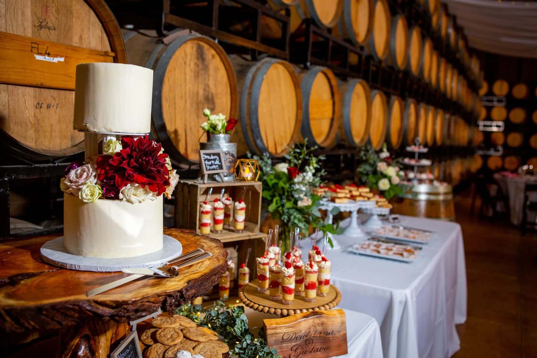 Wedding cake and dessert display beside rows of wine barrels