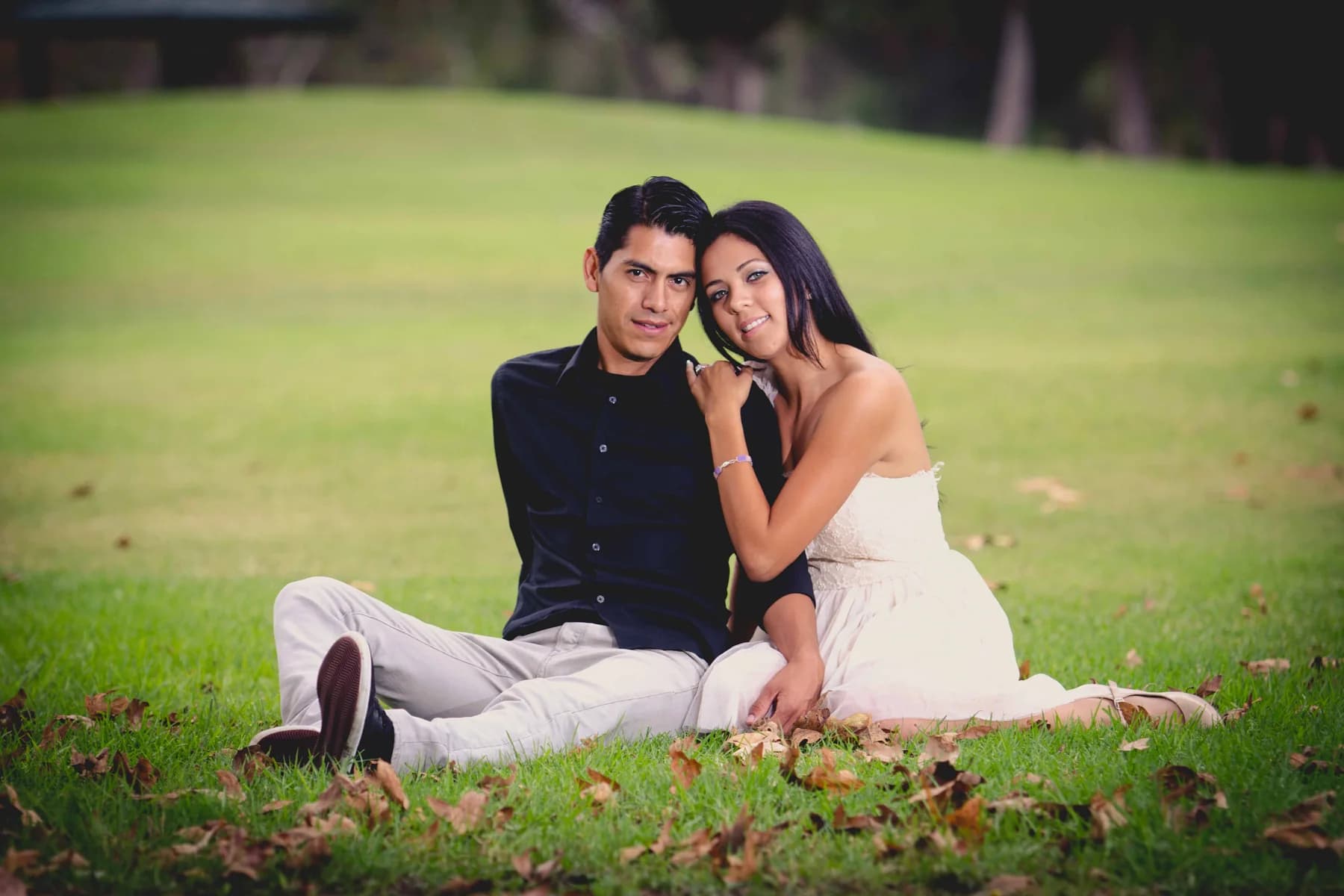 Couple seated together on grass beneath a shaded hillside