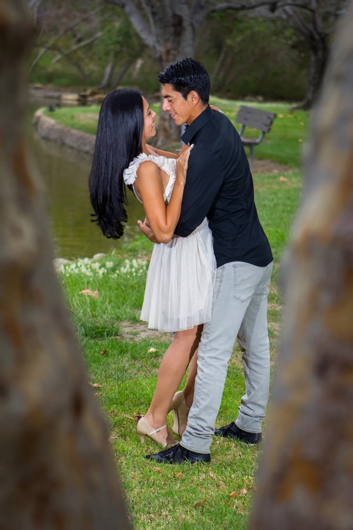 Couple smiling at each other while framed between two tree trunks
