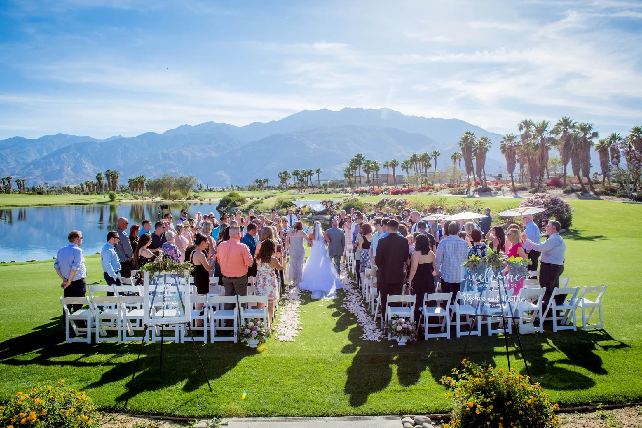 Outdoor wedding ceremony beside a lake with mountain and palm-tree views