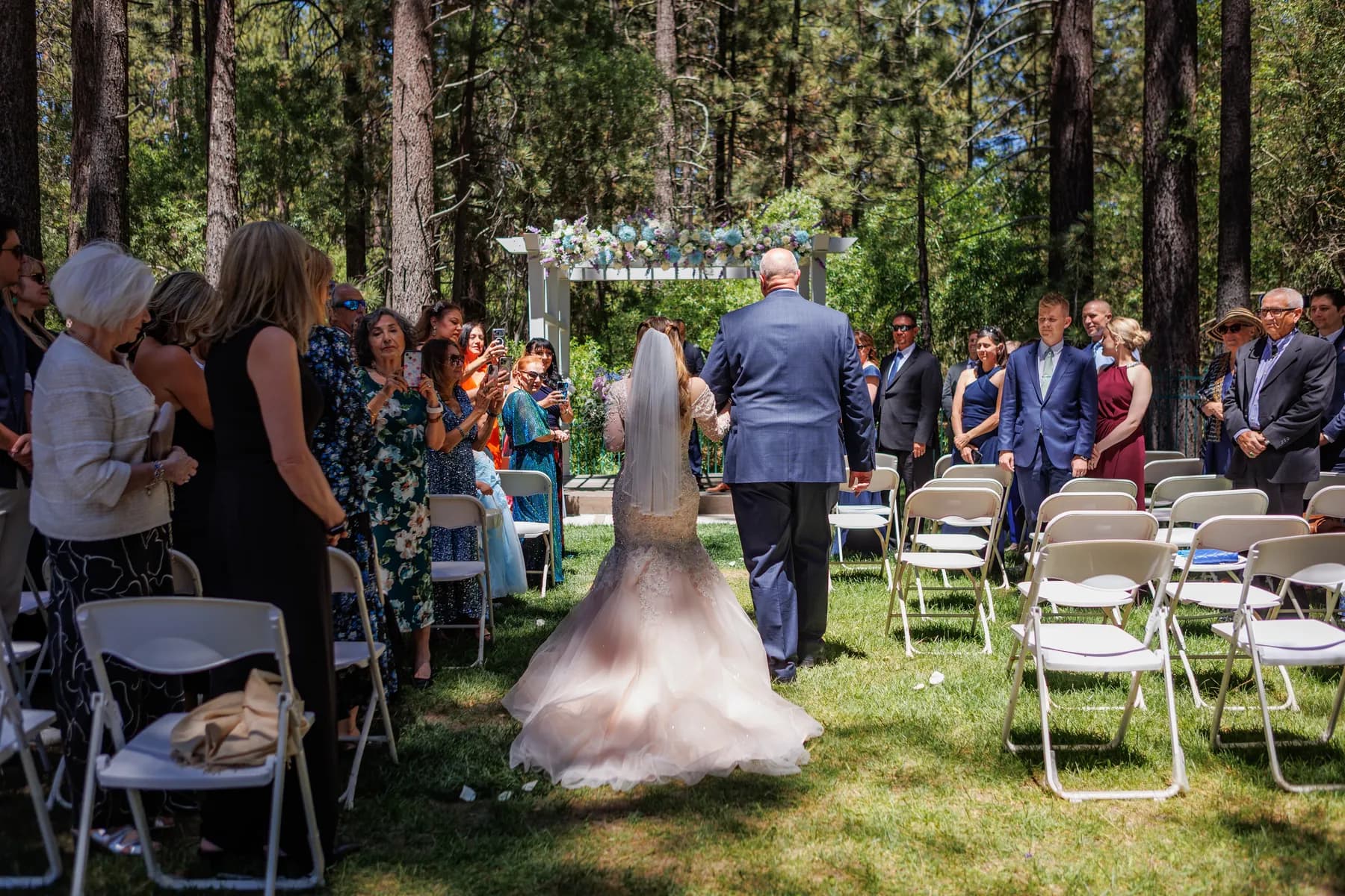 Guests watching Gloria walk down the outdoor aisle toward the arbor