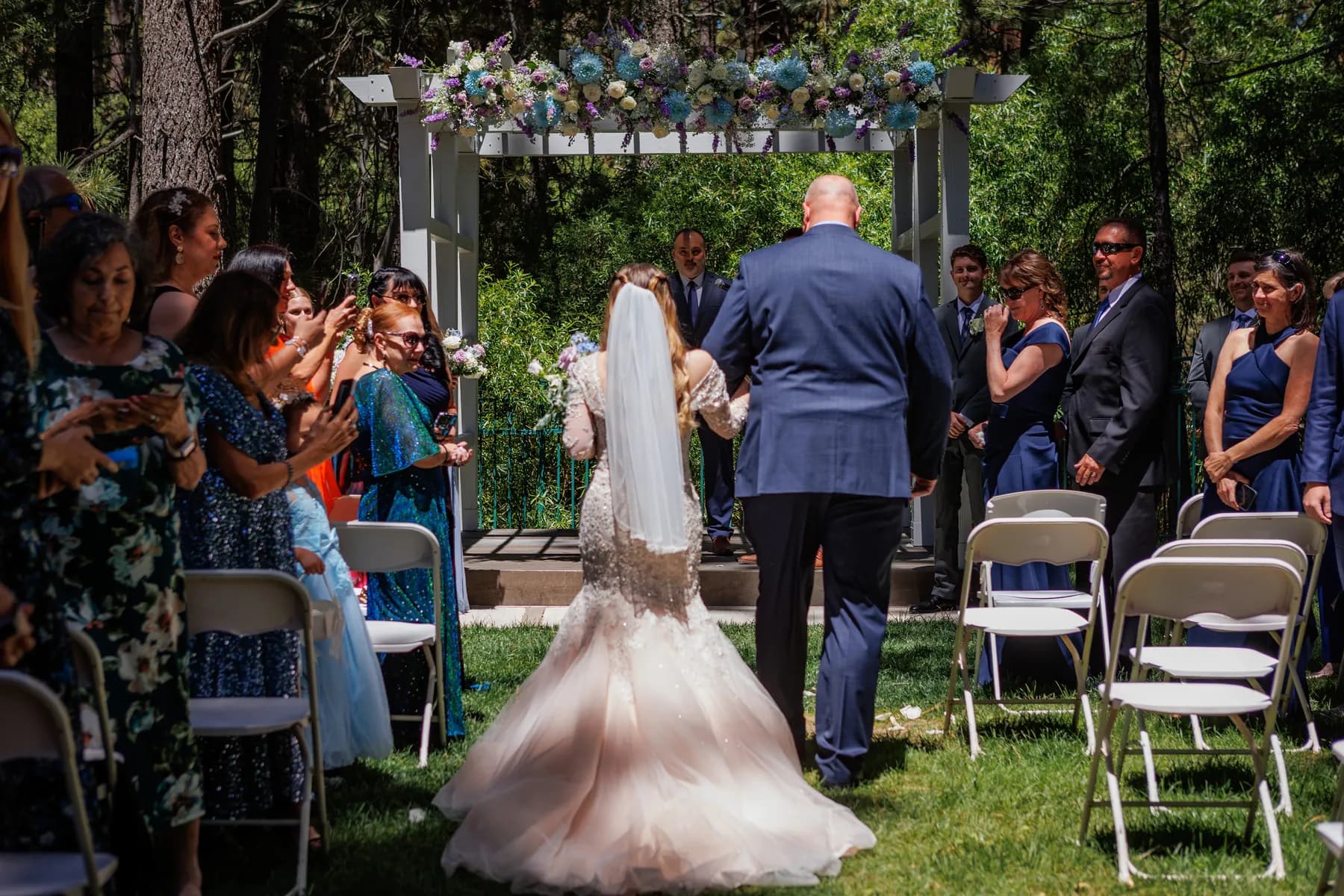 Gloria approaching the flower-covered arbor between rows of guests