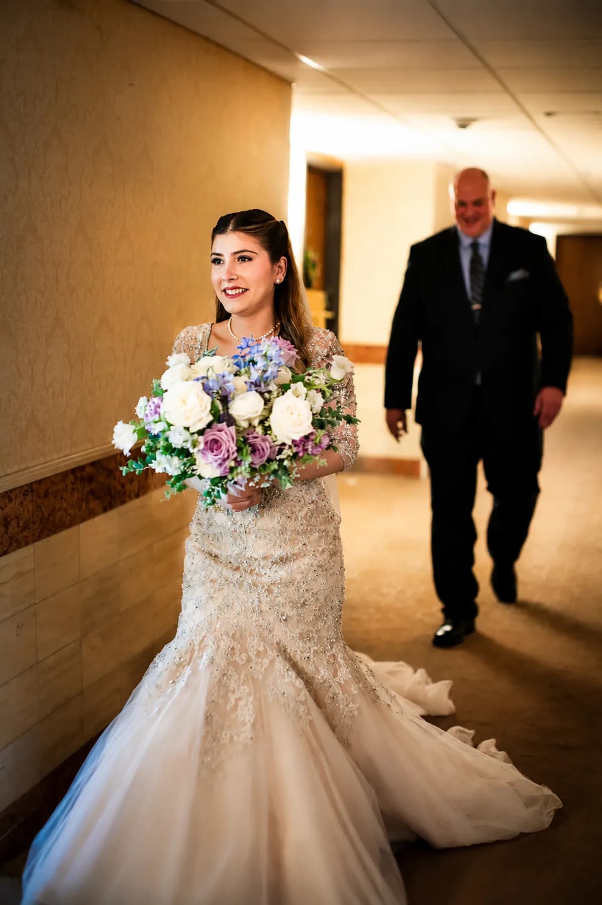 Gloria walking through a hallway with her bouquet and a companion nearby