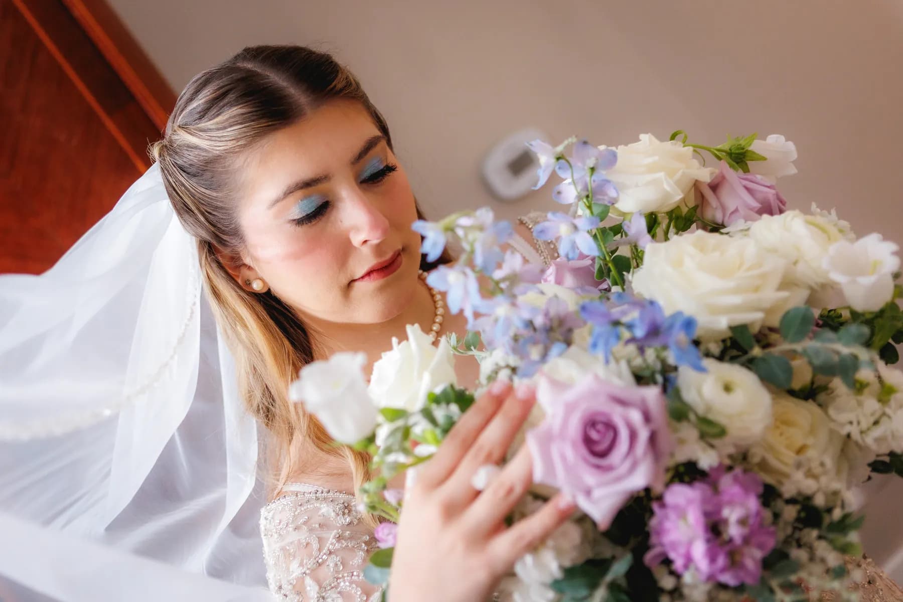 Gloria looking closely at her pale blue, lavender, and white bouquet