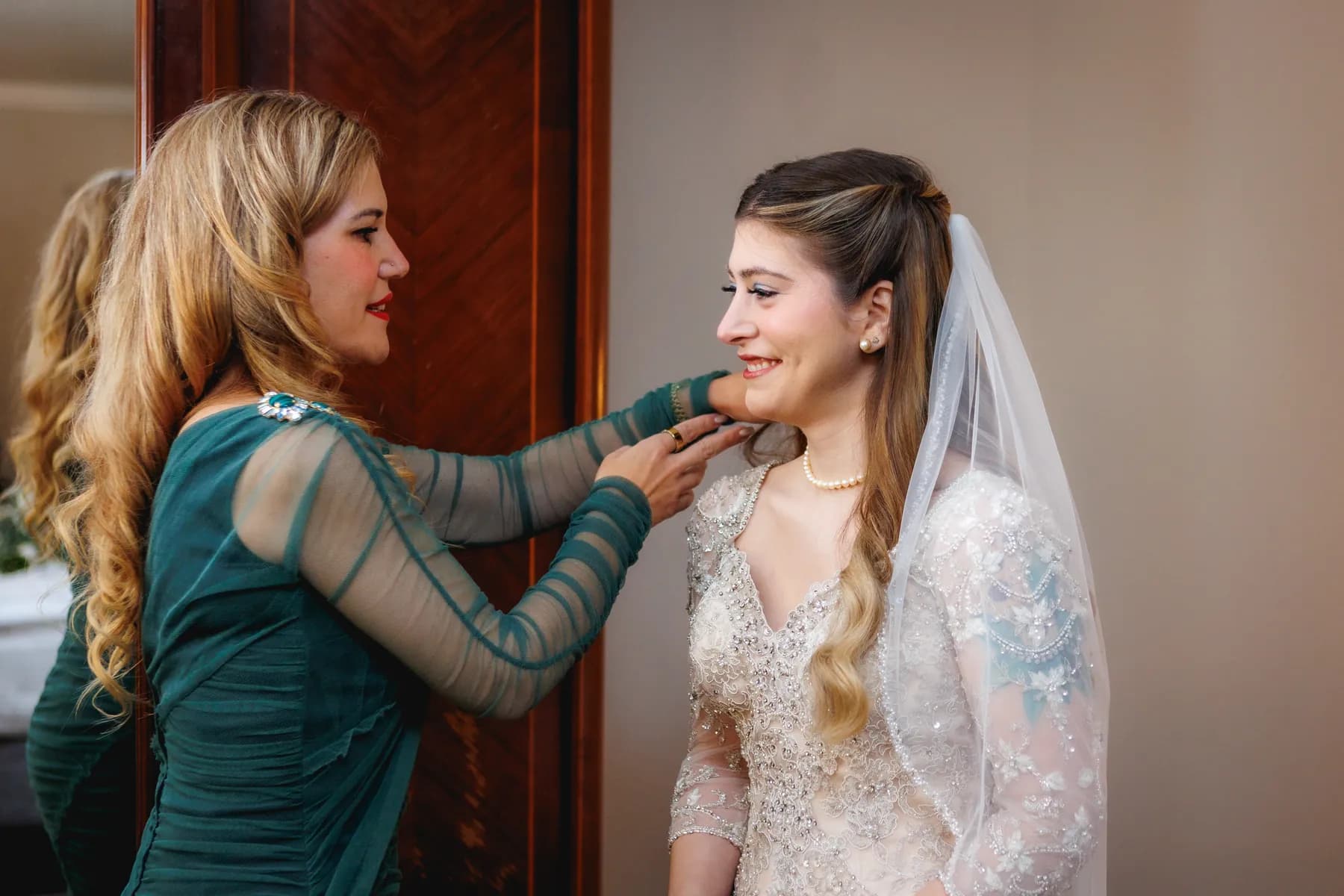 A companion adjusting Gloria's necklace during wedding preparations