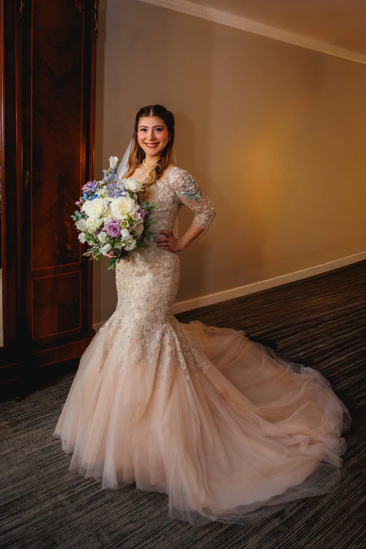 Gloria standing in her wedding dress and veil with a bouquet