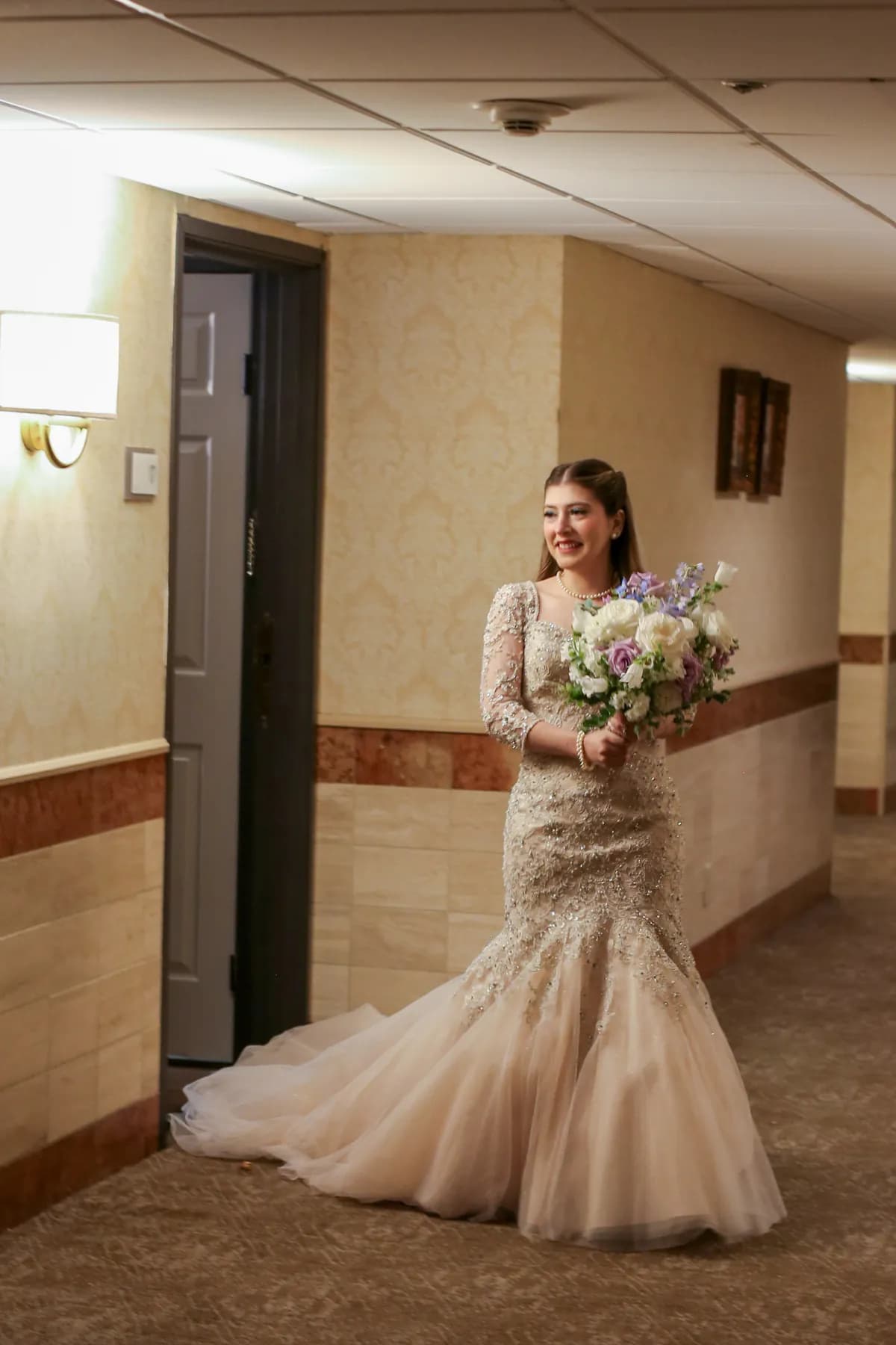 Gloria walking through a hallway carrying her bouquet