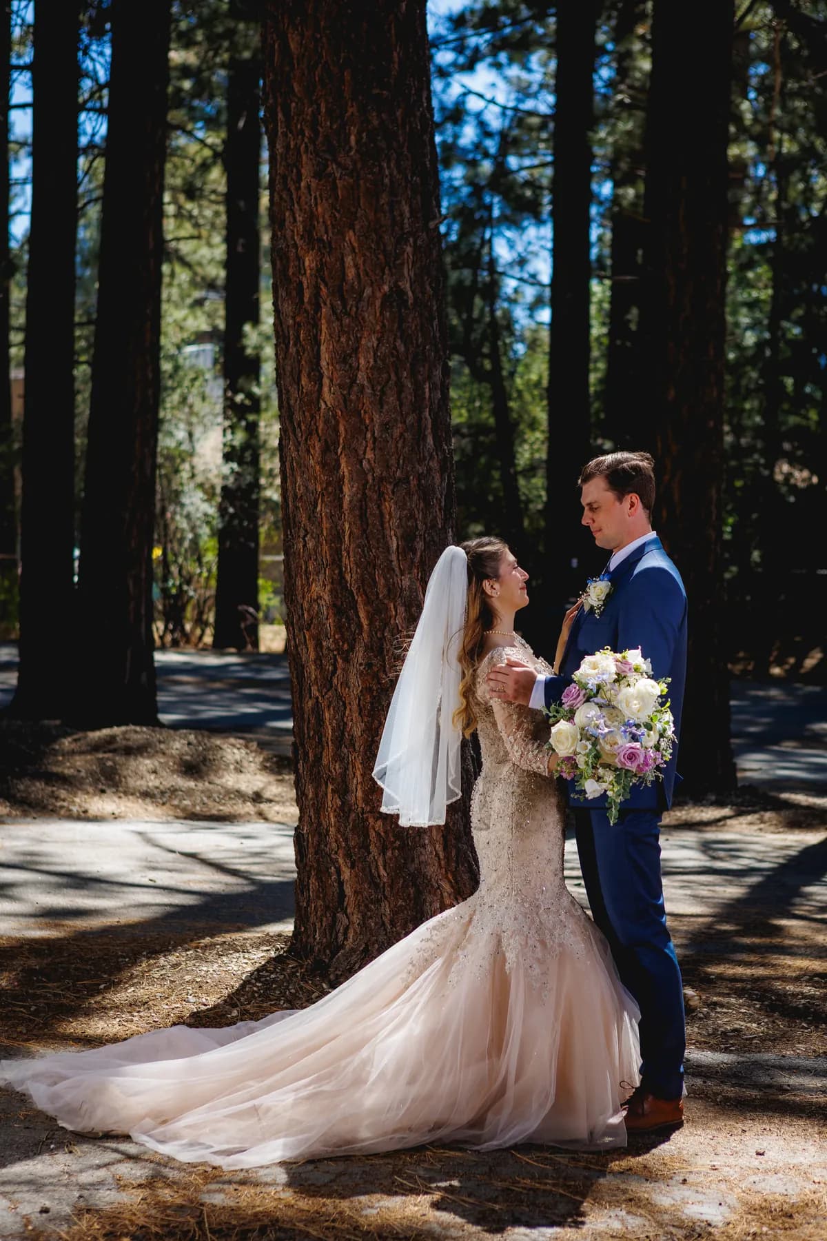 Gloria and Ryan standing together beside a tall pine trunk