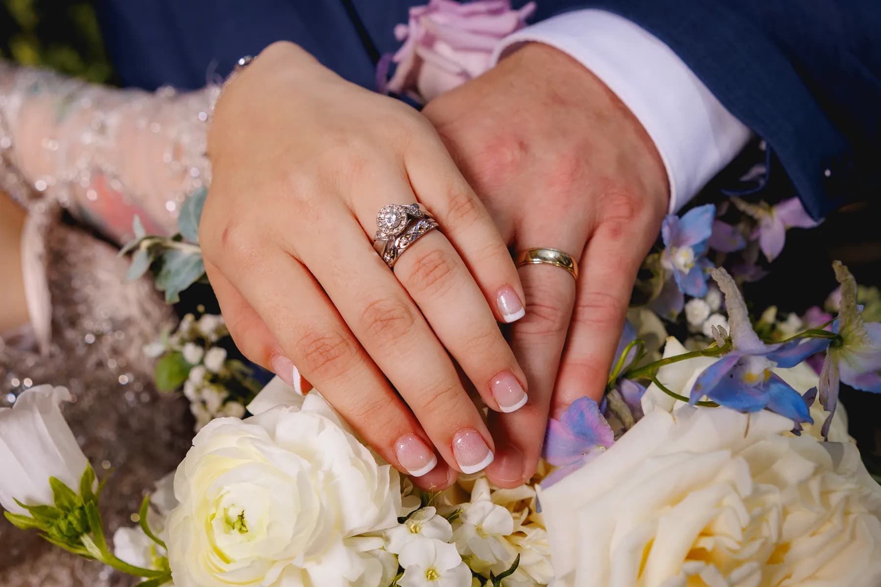 Close view of Gloria and Ryan's hands and wedding rings over pale flowers