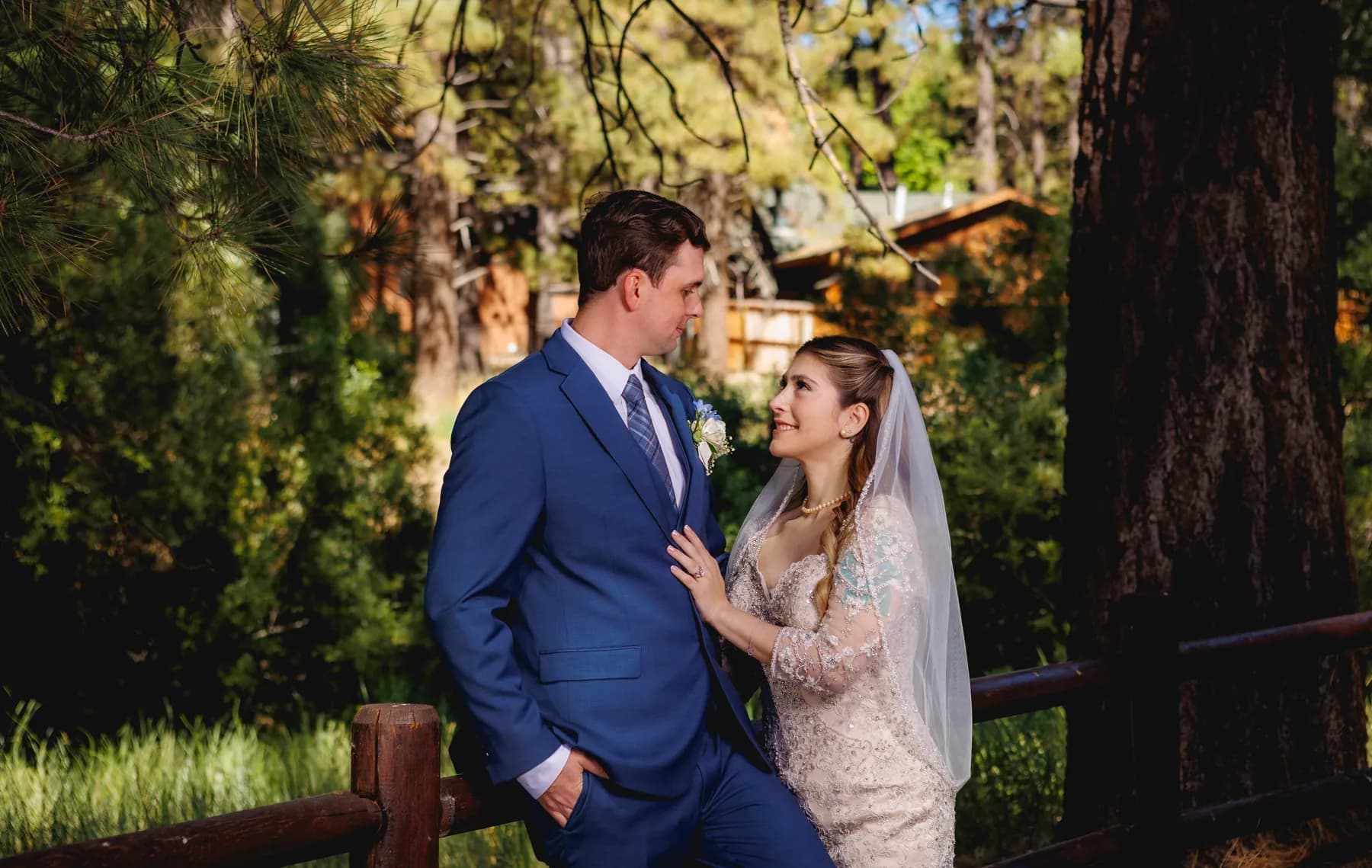 Gloria and Ryan facing one another by a wooden fence in dappled light