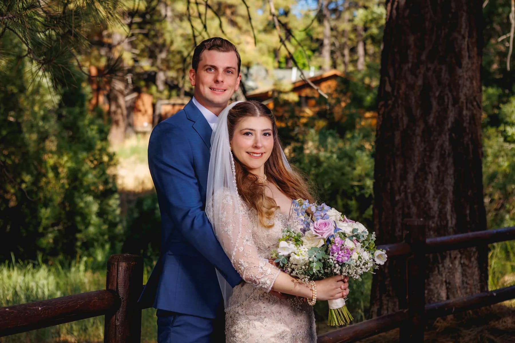 Gloria and Ryan standing close together with a bouquet against the trees