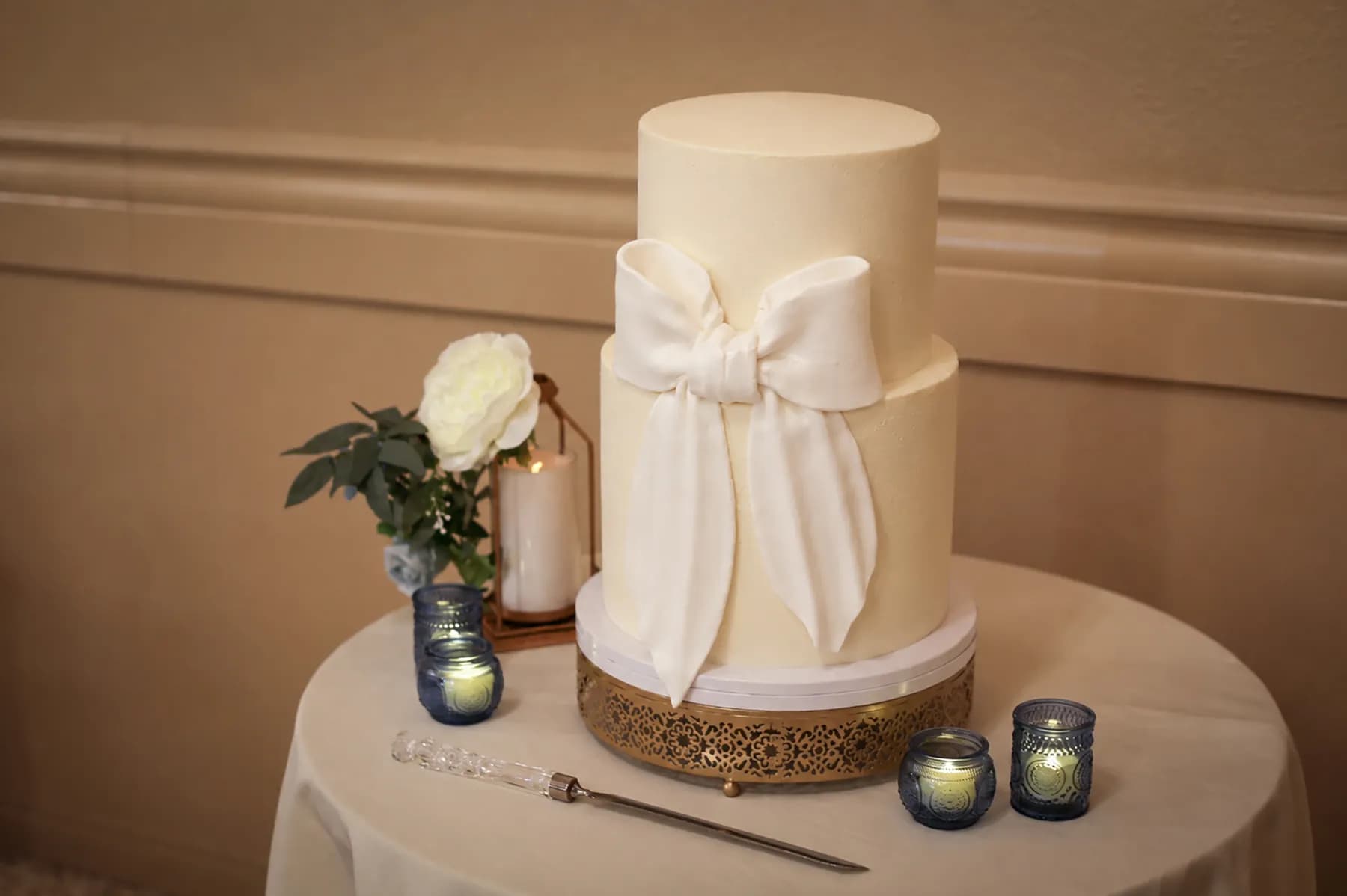 White tiered wedding cake with a ribbon and flower beside it