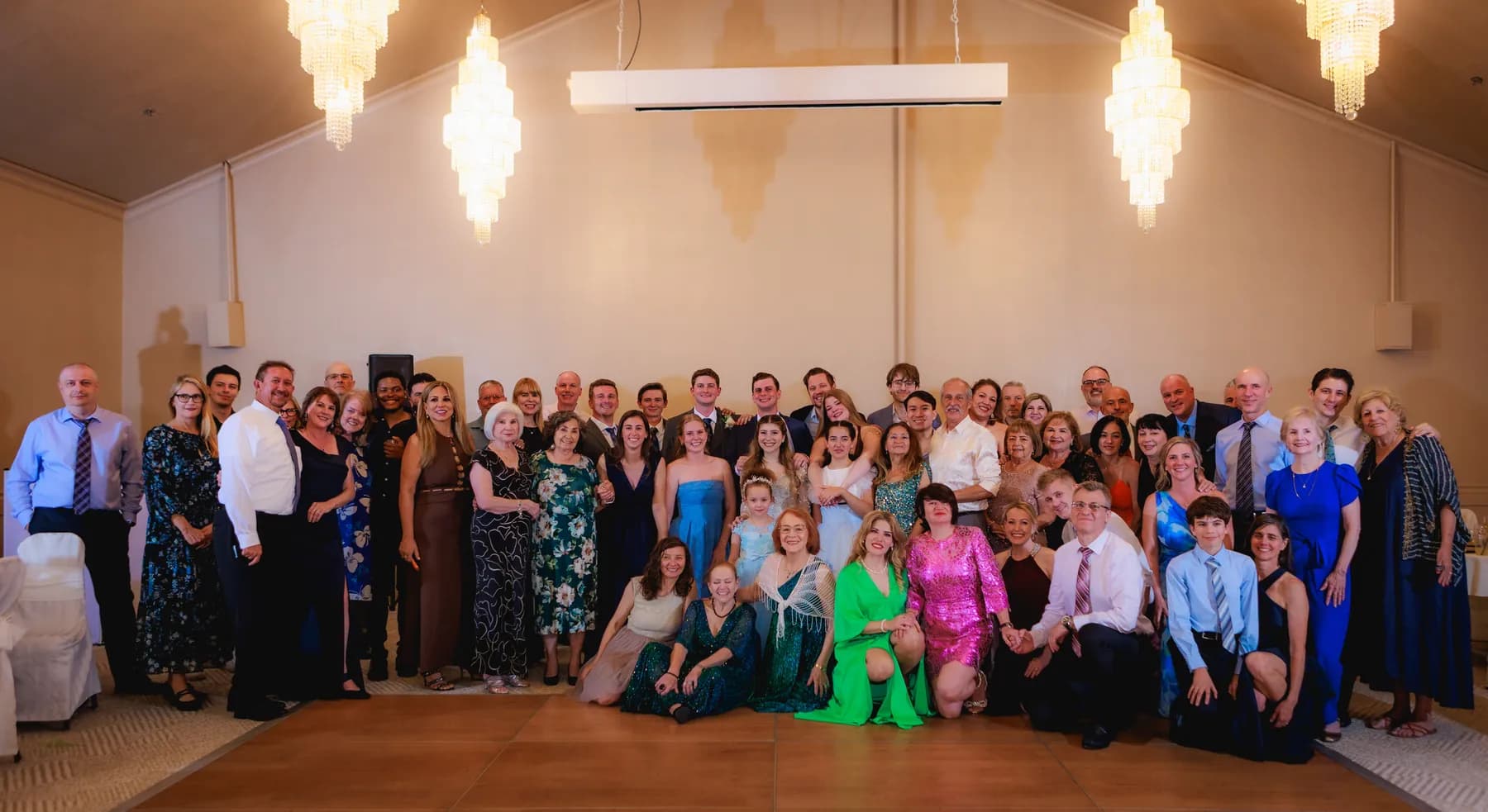 Large group of guests posing beneath reception chandeliers