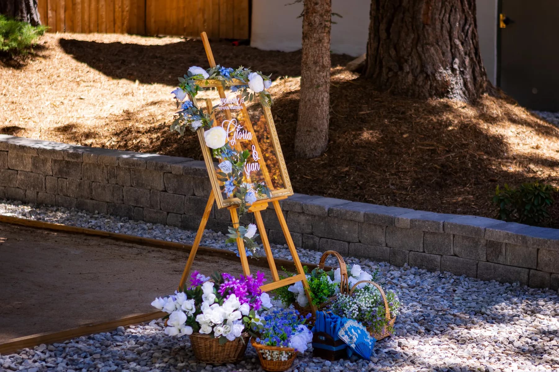 Flower-decorated welcome sign on an easel beside pine trees