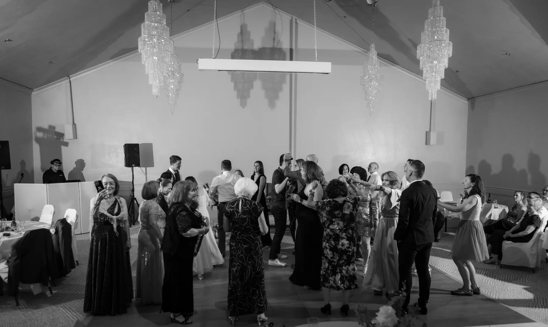 Black-and-white photograph of guests dancing beneath reception chandeliers
