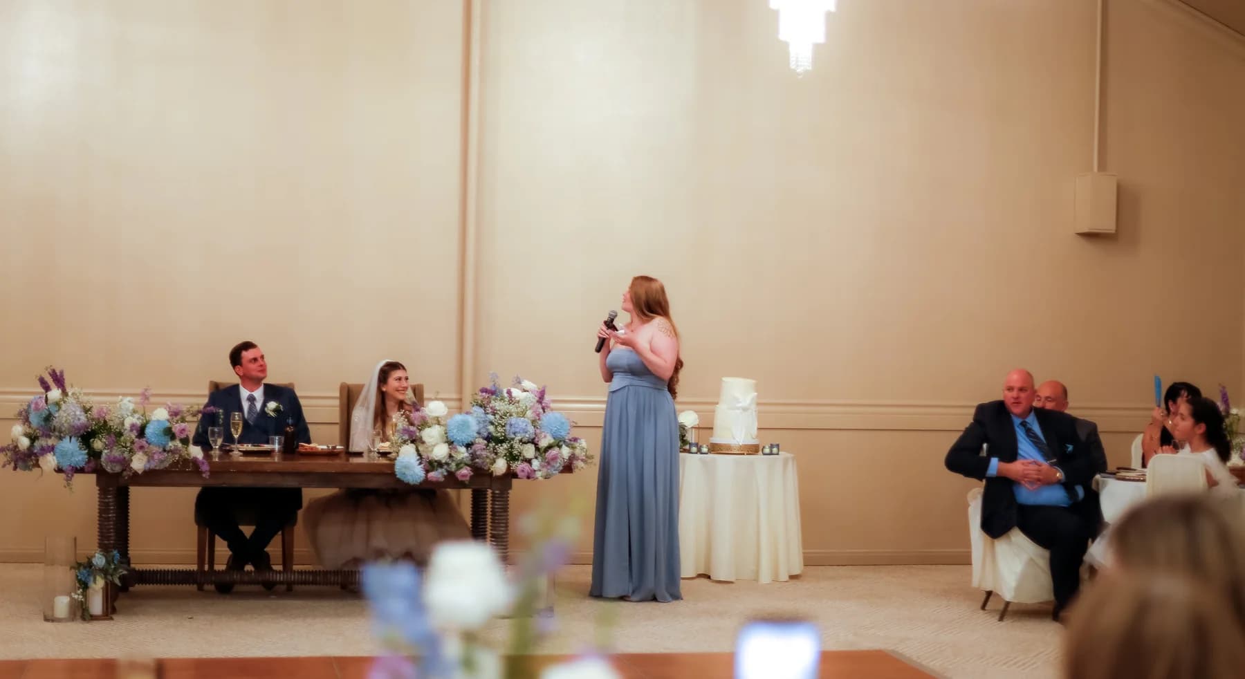 A guest giving a toast while Gloria and Ryan sit at the reception table