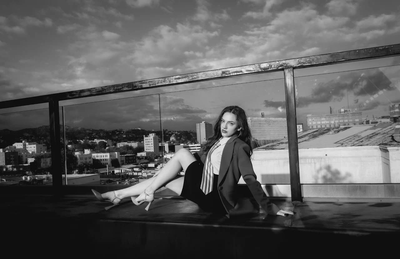 Black-and-white seated fashion portrait beneath clouds