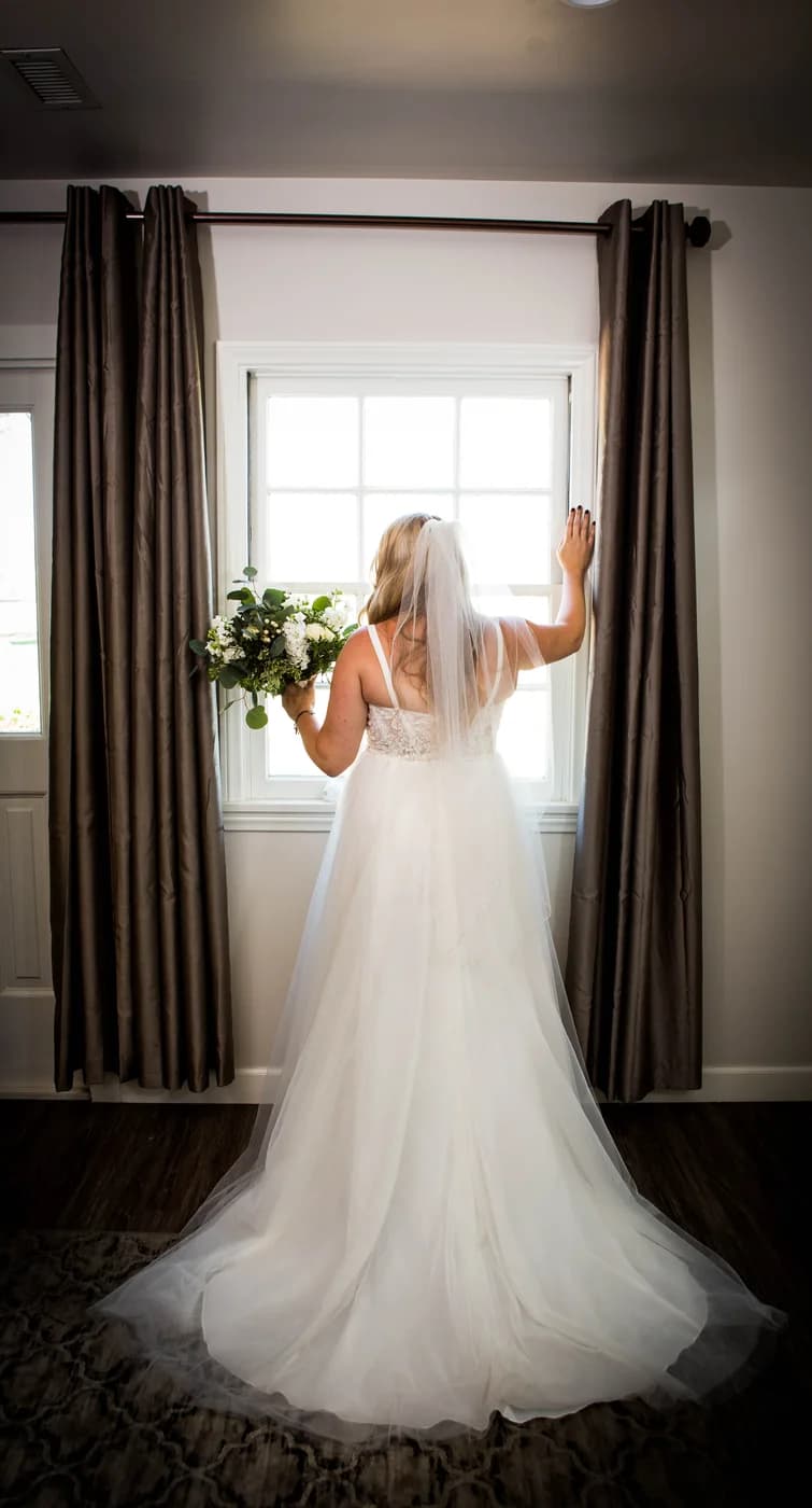 Bride holding her bouquet while looking through a window before the ceremony